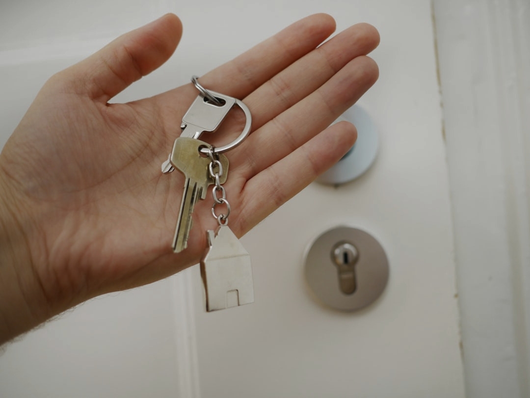 A hand holding house keys with a home-shaped keychain, representing simplified residential real estate investing through Aspen Sage Investment Fund.